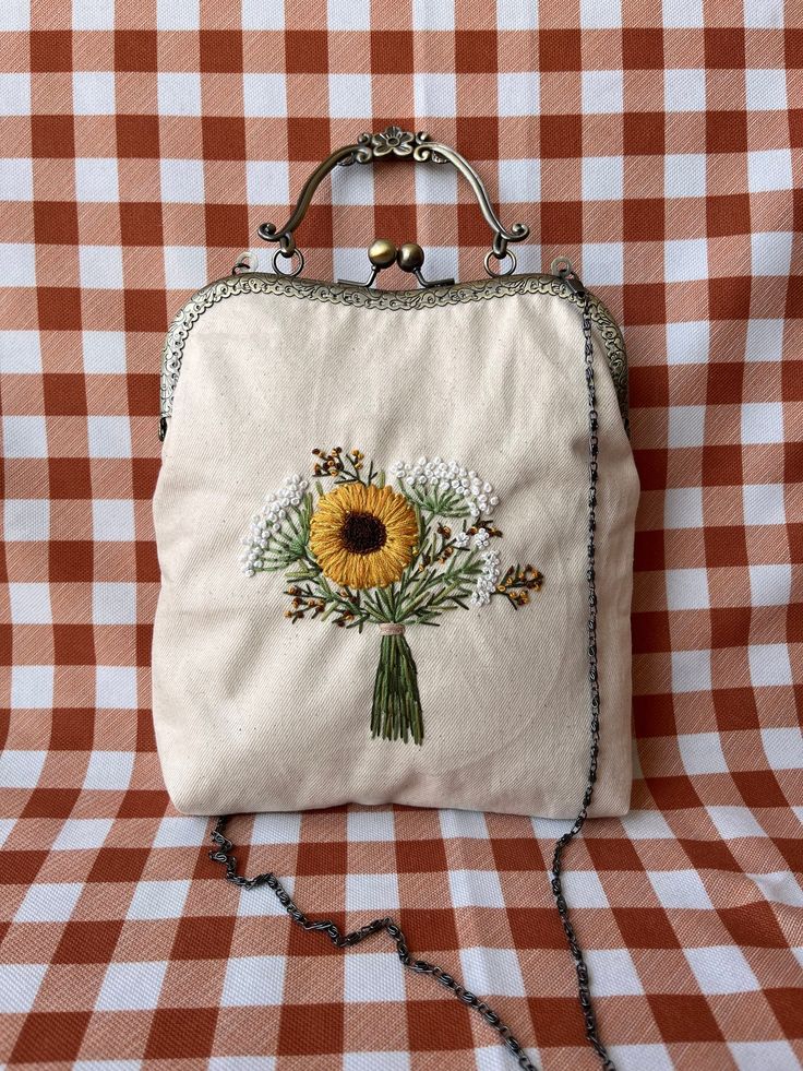 a white purse with a sunflower on it sitting on a checkered table cloth