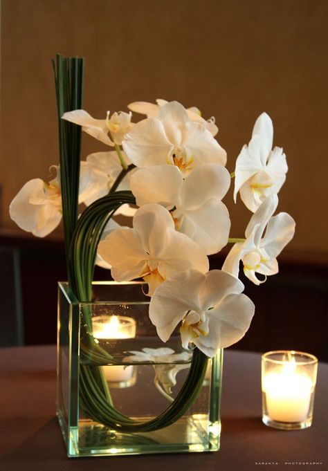 a vase filled with white flowers sitting on top of a table next to a candle