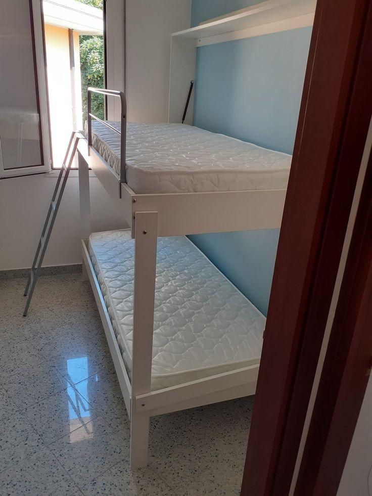 two bunk beds in a small room with blue walls and white flooring, one is closed to the other side