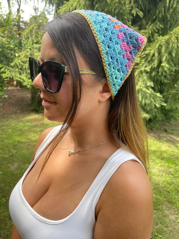 a woman wearing sunglasses and a crocheted hat in front of green grass with trees