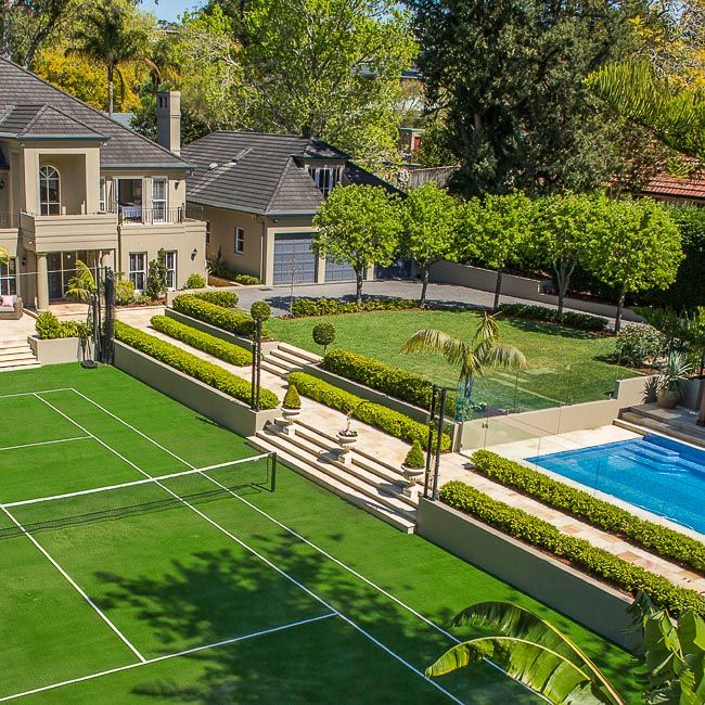 an aerial view of a tennis court and pool in front of a large house with landscaping