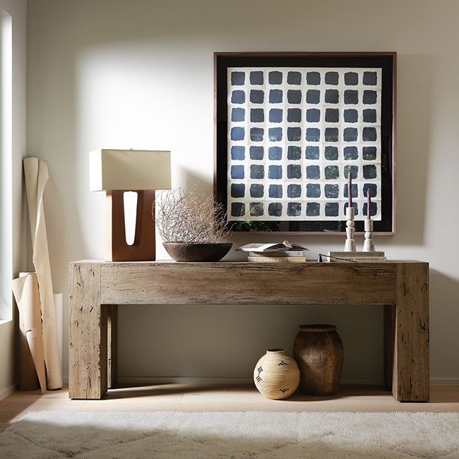 a wooden table with vases on it in front of a wall mounted art piece