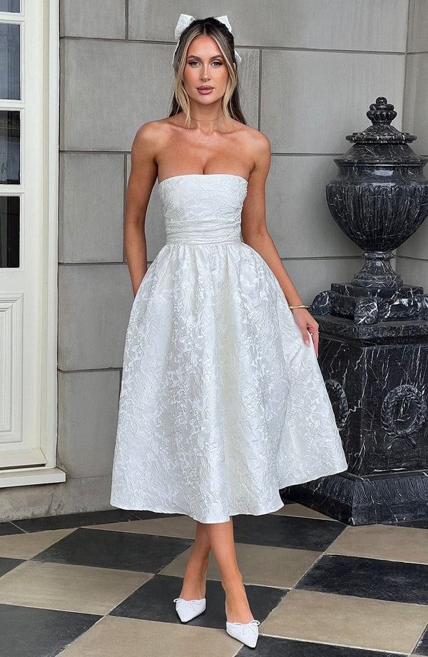 a woman standing in front of a building wearing a white dress