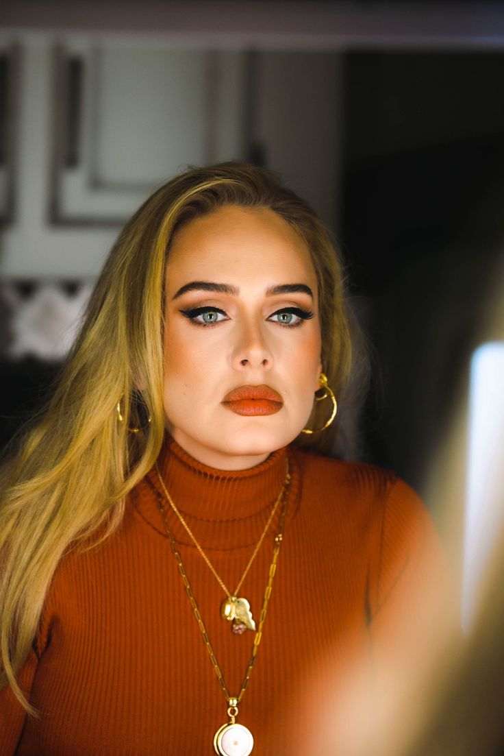 a woman with long blonde hair and blue eyes wearing gold hoop earrings is looking at her reflection in the mirror