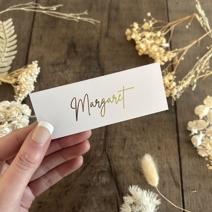 a person holding up a business card with the word margart on it in gold foil