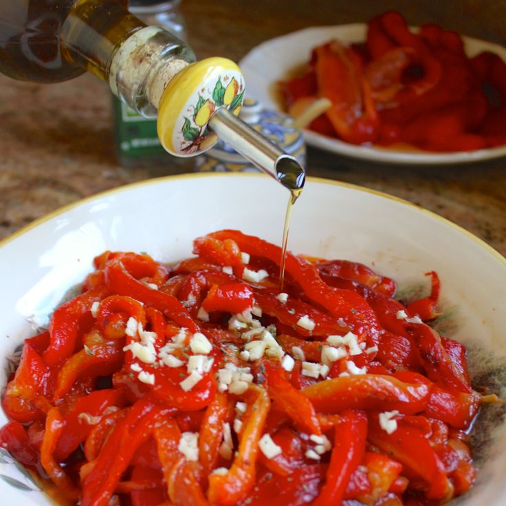 a white bowl filled with red bell peppers and seasoning being drizzled over them