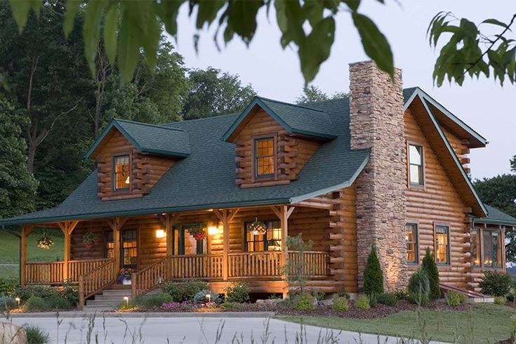 a log home with green roofing and lights on the front porch is lit up at night