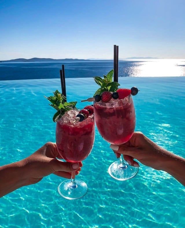 two people holding up wine glasses with strawberries and berries on them in front of the ocean