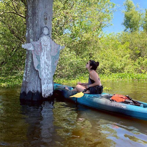 a woman sitting on top of a blue kayak next to a tree in the water