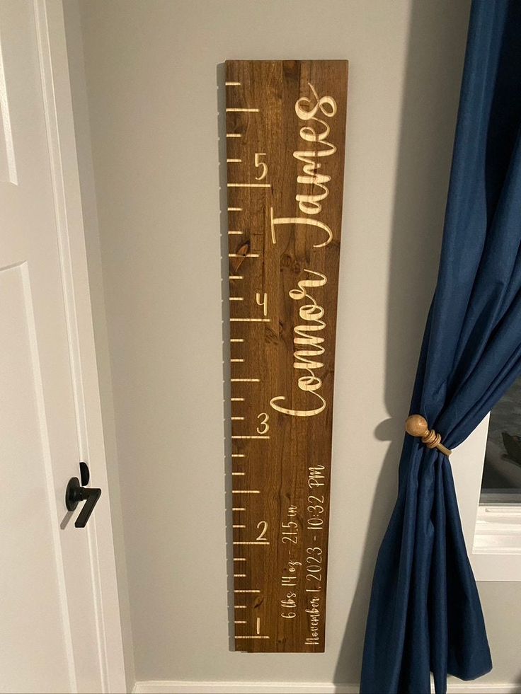 a wooden growth chart hanging on the wall next to a window with blue drapes