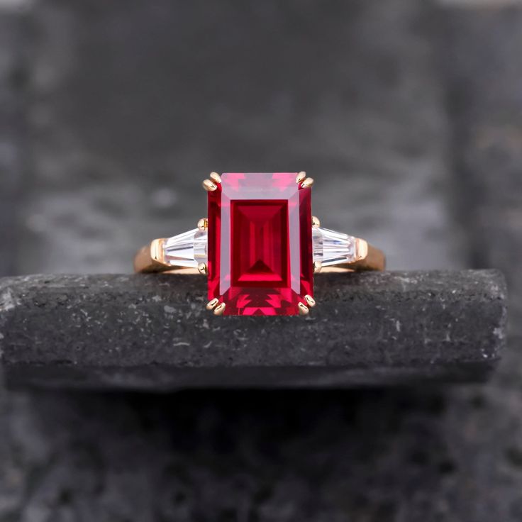 a red and white diamond ring sitting on top of a rock