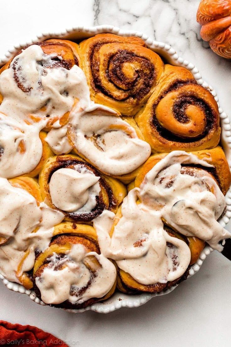 cinnamon rolls with cream cheese frosting in a white dish on a marble counter top