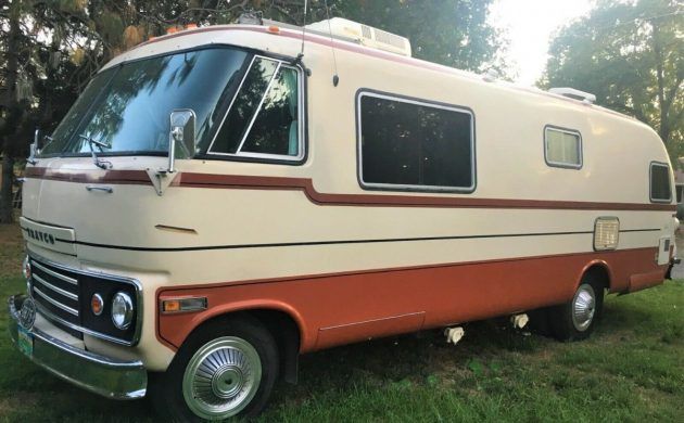 an orange and white motor home parked in the grass