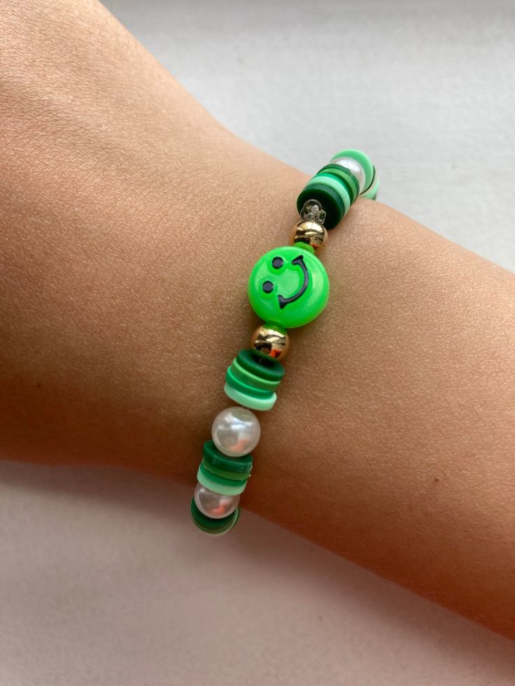 a woman's arm with a green and white beaded bracelet that has a smiley face on it