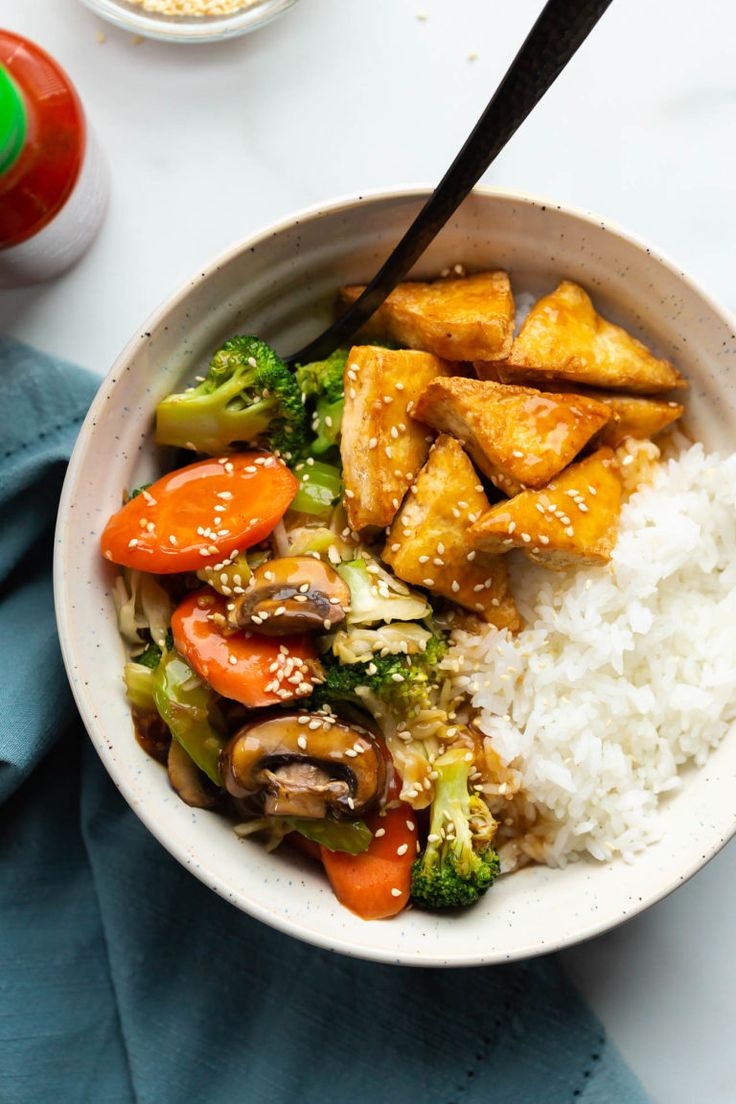 a bowl filled with rice, broccoli and tofu on top of a table