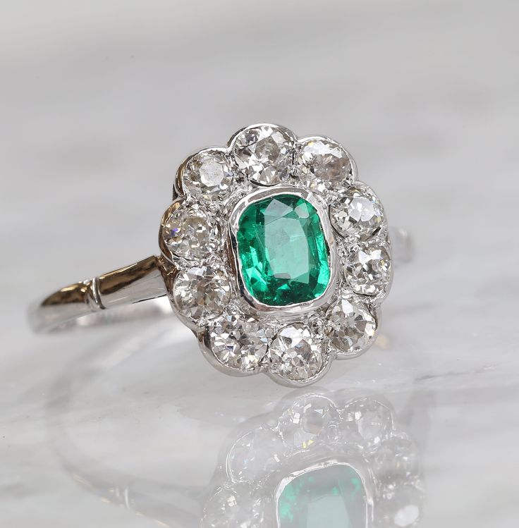 Here we have a stunning Art Deco emerald and diamond Cluster Ring. The ring features a central cushion cut emerald that is a perfect rich green colour with a great clarity. The emerald is highly complimented by the contrasting bright white sparkle of the surrounding ten old cut diamonds. It is crafted in 18ct white gold and has a low profile making it perfect for everyday wear. Condition: Used (Excellent) Weight: 2.6 grams Ring Size: Q (58) Face Dimensions: 13.5mm x 12mm Emerald: Approx. 0.75 ca Luxury Green Cluster Ring With Center Stone, Classic Green Cluster Diamond Ring, Classic Green Diamond Cluster Ring, Fine Jewelry Emerald Ring With Cushion Cut Diamond, Emerald Cluster Ring With Diamonds, Green Emerald Cluster Ring With Brilliant Cut, Cluster Green Emerald Ring For Wedding, Green Emerald Cluster Ring With Diamonds, Platinum Green Diamond Ring