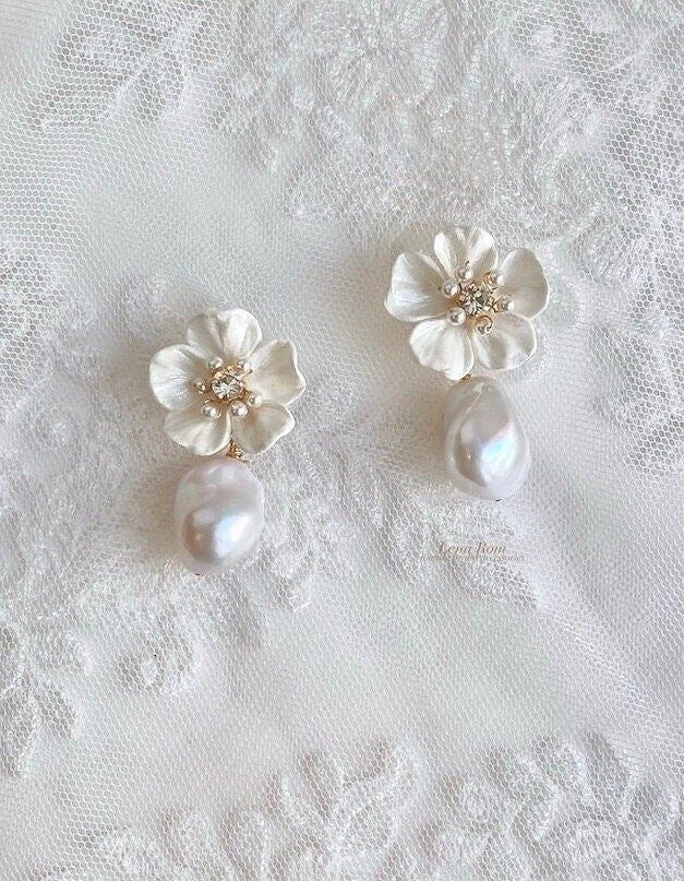 two white flowers and pearls are on top of a lace tablecloth, next to a pair of earrings