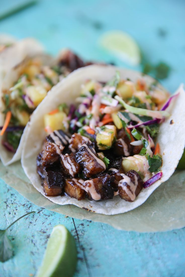 two tacos filled with meat and veggies sitting on top of a table