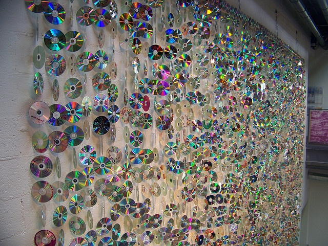 a wall covered in lots of different colored cds on it's side and hanging from the ceiling