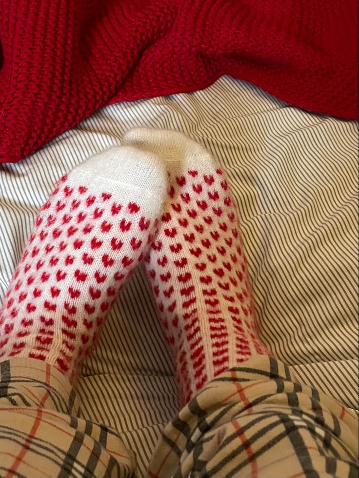 the legs of a person wearing red and white socks with hearts on them are laying on a bed