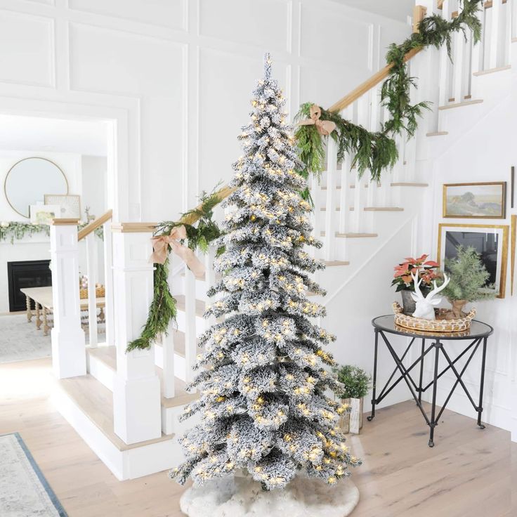 a decorated christmas tree in the middle of a room with stairs and pictures on the wall