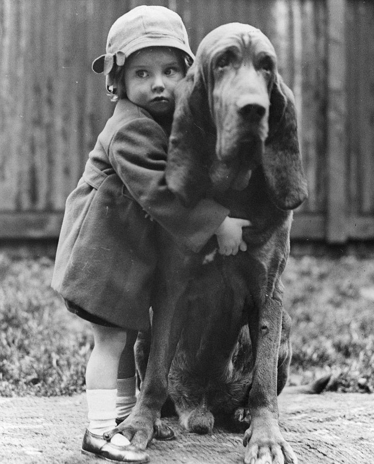 an old black and white photo of a child hugging a dog