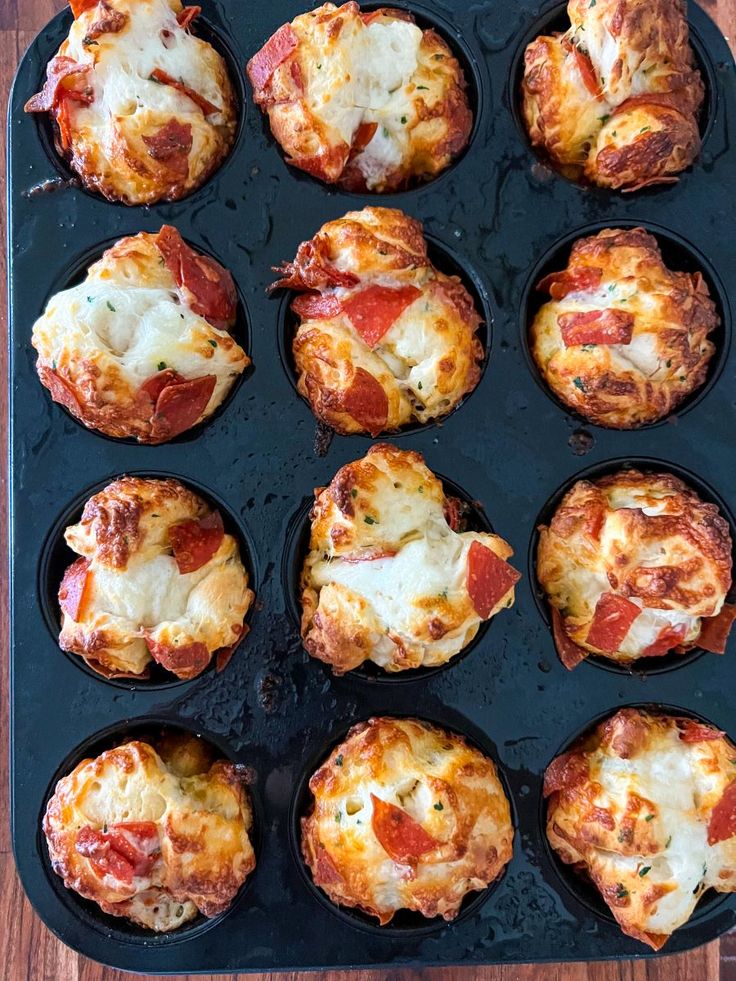 a muffin tin filled with mini pizzas on top of a wooden table