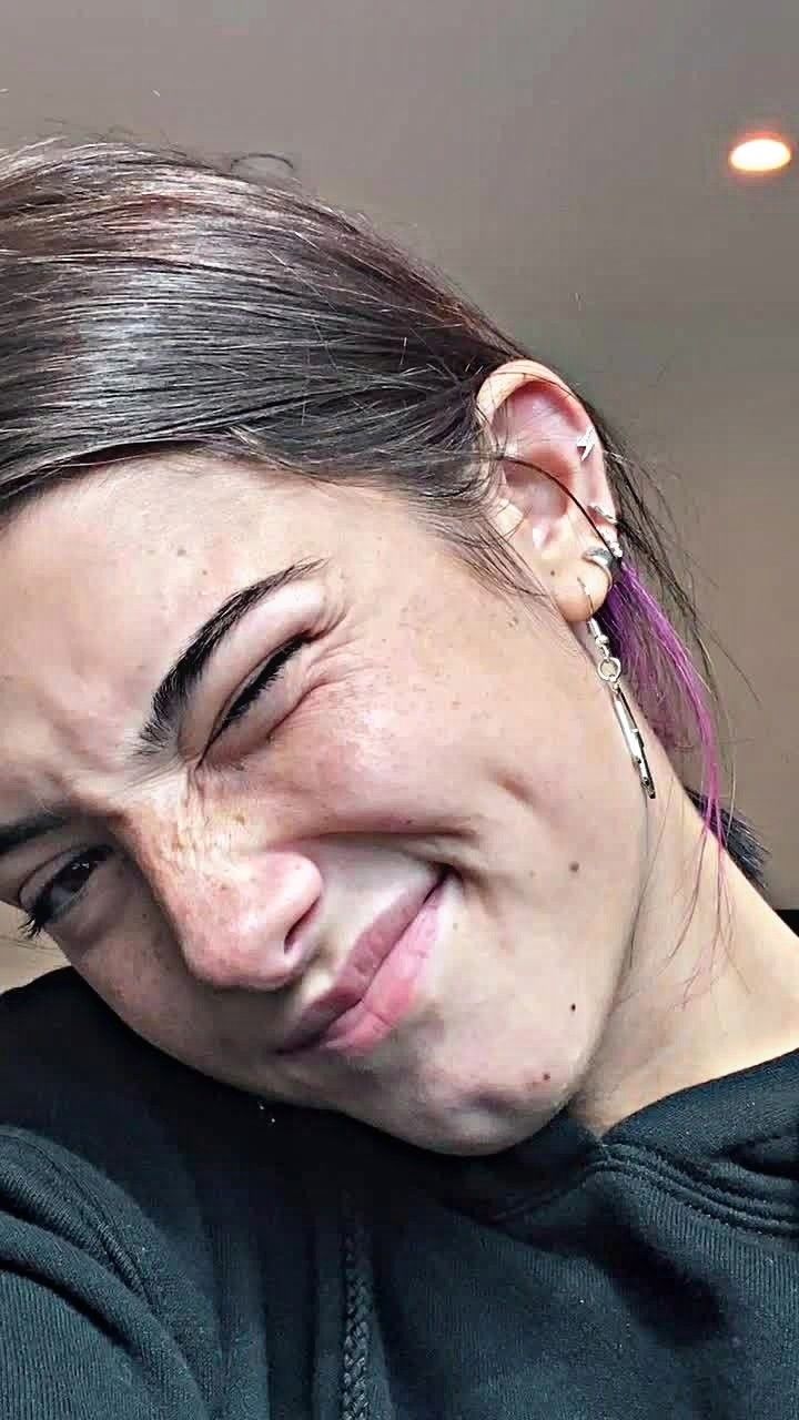 a woman with her eyes closed and ear piercings in front of her face smiling