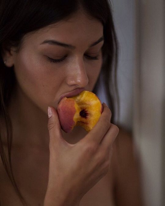 a naked woman eating an apple with her right hand