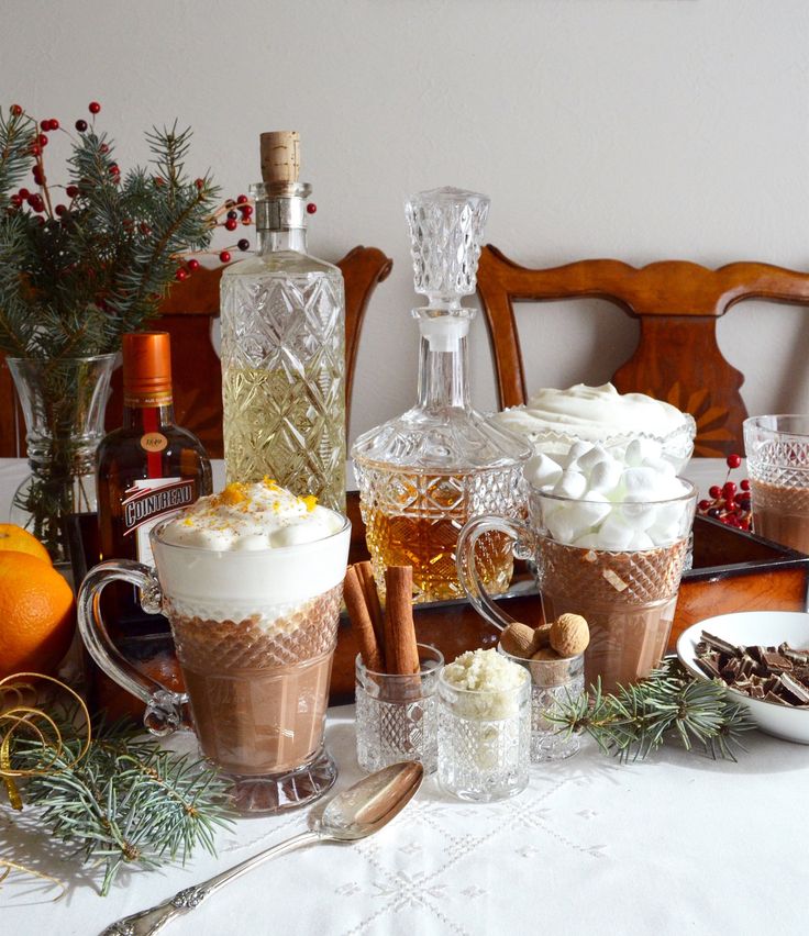 a table topped with cups filled with drinks and desserts next to bottles of alcohol