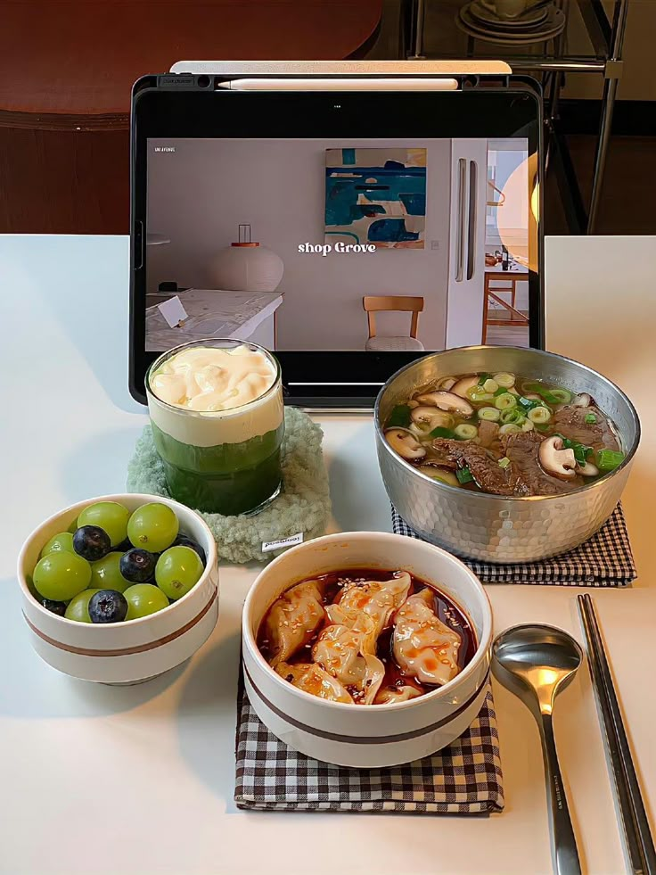 a laptop computer sitting on top of a table next to bowls of food