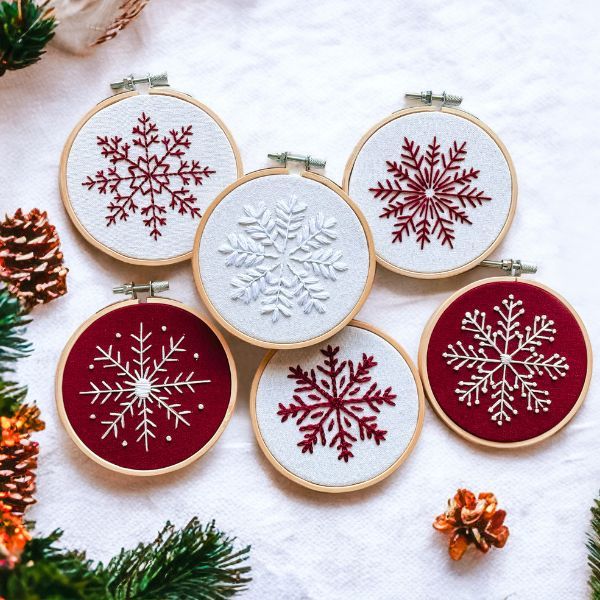 four cross stitch snowflakes are displayed in front of pine cones and evergreen branches