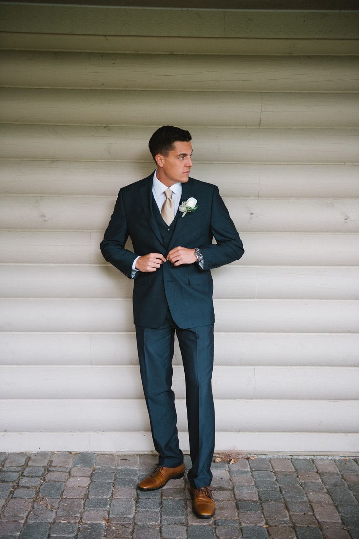 a man in a suit and tie standing next to a wall with his hands in his pockets