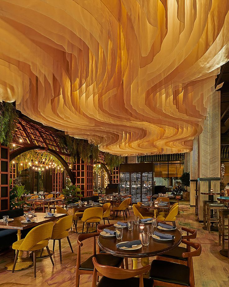 a restaurant with wooden tables and yellow chairs, hanging lights above the dining room area