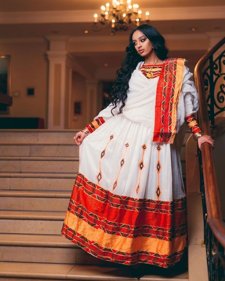 This exquisite Ethiopian Habesha dress is a true masterpiece of traditional craftsmanship. The lower part of the dress is made of Shimena, which is handwoven with great care and attention to detail, resulting in a beautiful and unique texture. The Menen fabric used in this dress is of the highest quality, adding a luxurious feel to the overall design. The neckline and wrists of the dress are adorned with intricate Tilf embroidery, adding an elegant and sophisticated touch to the vibrant colors o Traditional Festive Dress With Woven Motifs, Anarkali Dress With Woven Motifs For Traditional Ceremonies, Floor-length Maxi Dress With Traditional Patterns For Festivals, Festive White Dress With Weaving Work, Transitional Festive Dresses With Woven Motifs, Wedding Dress With Woven Motifs For Transitional Season, Transitional Wedding Dress With Woven Motifs, Fitted Wedding Dress With Woven Motifs, Traditional Dress With Woven Motifs For Festive Occasions