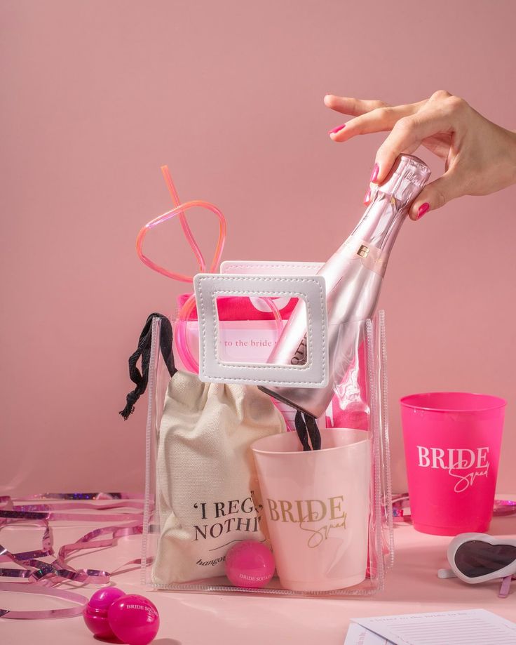 a pink table topped with lots of personal items and a hand holding a wine bottle