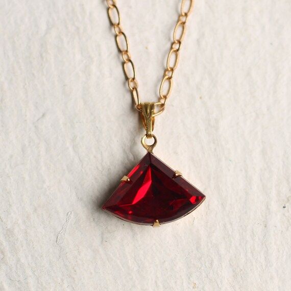 This beautifully simple necklace is faceted vintage glass in a rich and vibrant ruby red shade.   The classic fan shape of the stone is reminiscent of Art Deco in its simplicity and strong lines, and the glass has been foiled with gold from behind, so it really catches the light beautifully. The ruby fan jewel measures 20mm (just less than one inch) wide so is a great, versatile size for shorter and mid length chains.  We offer a variety of chain lengths.  Please check our illustration on this l Red Faceted Pendant Necklaces, Red Faceted Pendant Necklace, Vintage Red Gemstone Necklace, Red Gemstone Necklace For Party, Ruby Red Necklace, Red Art Deco, Art Deco Pendant Necklace, Ruby Jewel, Photo Locket Necklace