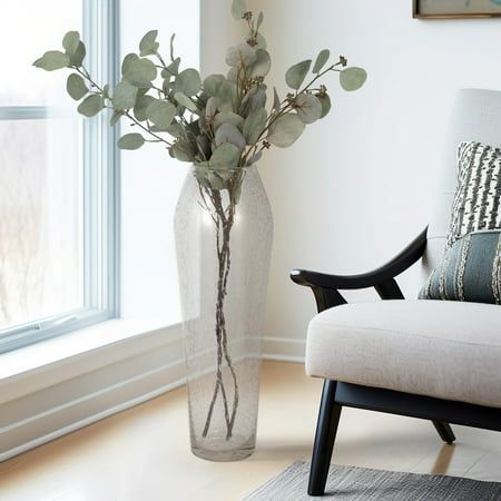 a living room with a chair and a vase on the floor next to a window