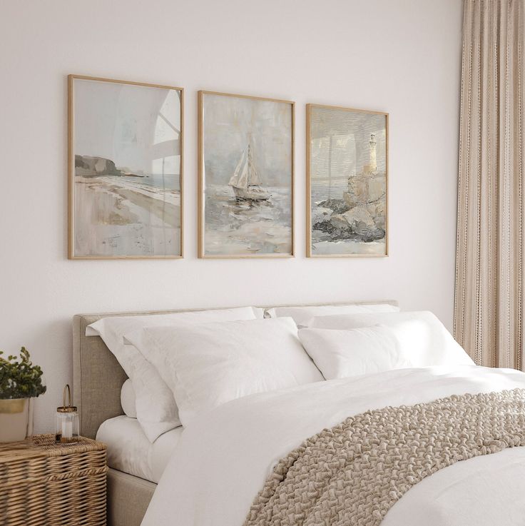 a bed with white linens and two paintings on the wall above it, along with a wicker basket