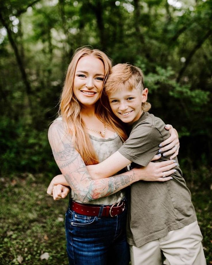 a woman hugging a boy with tattoos on his arms in the middle of a forest