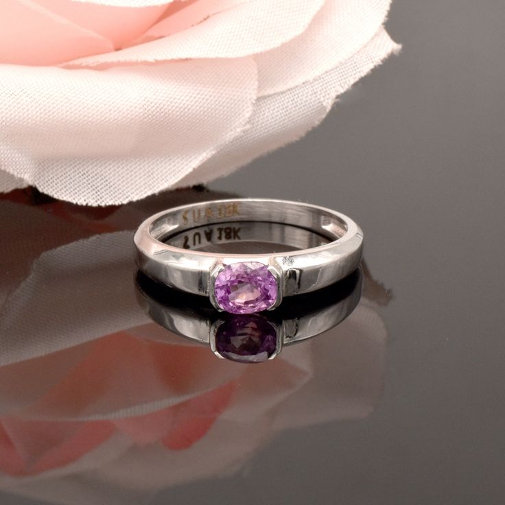 a pink rose sitting on top of a table next to a silver ring with purple stones