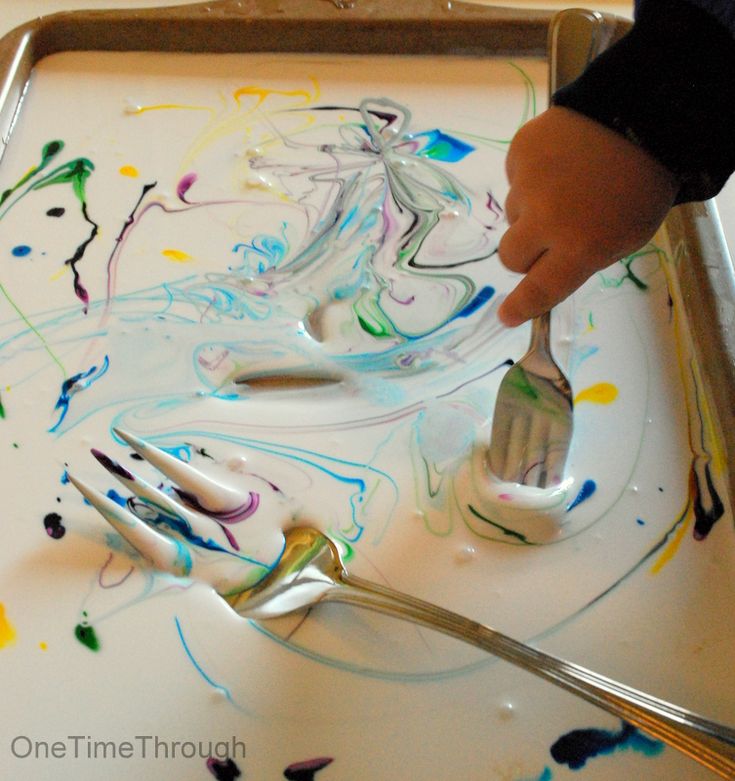 a child's hand is holding a spoon and fork in front of paint on a tray