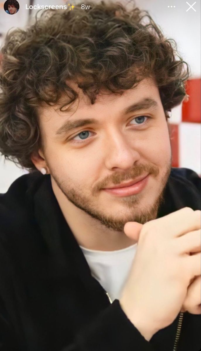 a close up of a person with curly hair and blue eyes wearing a black jacket