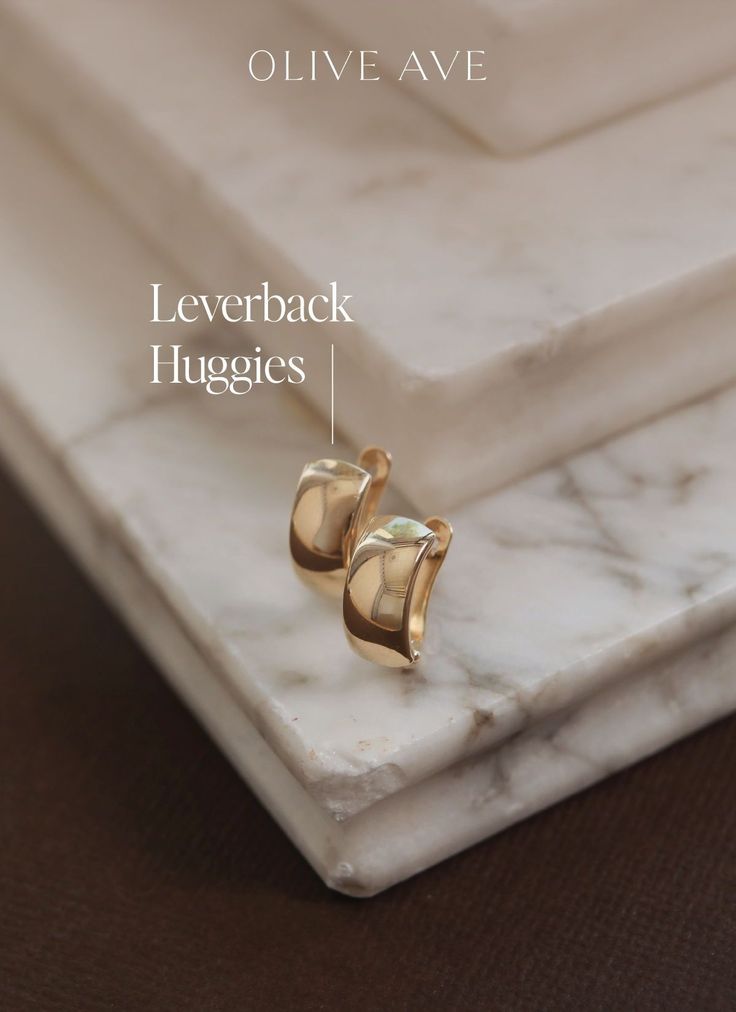 two gold rings sitting on top of a white marble slab with the words leverback huggies below it