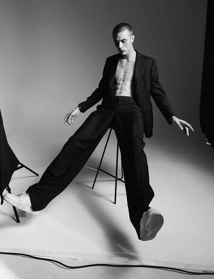 a man sitting on top of a chair in front of a white wall with his legs spread out