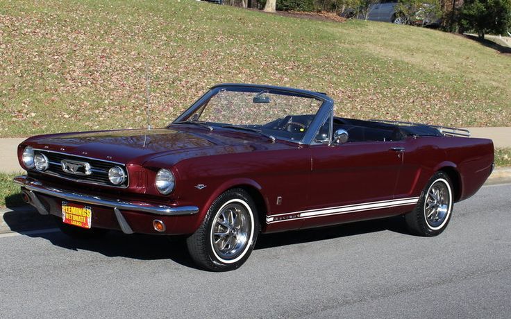 an old red mustang convertible parked on the side of the road