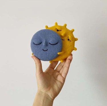 a hand holding up a small yellow and blue toy with a sleeping face on it