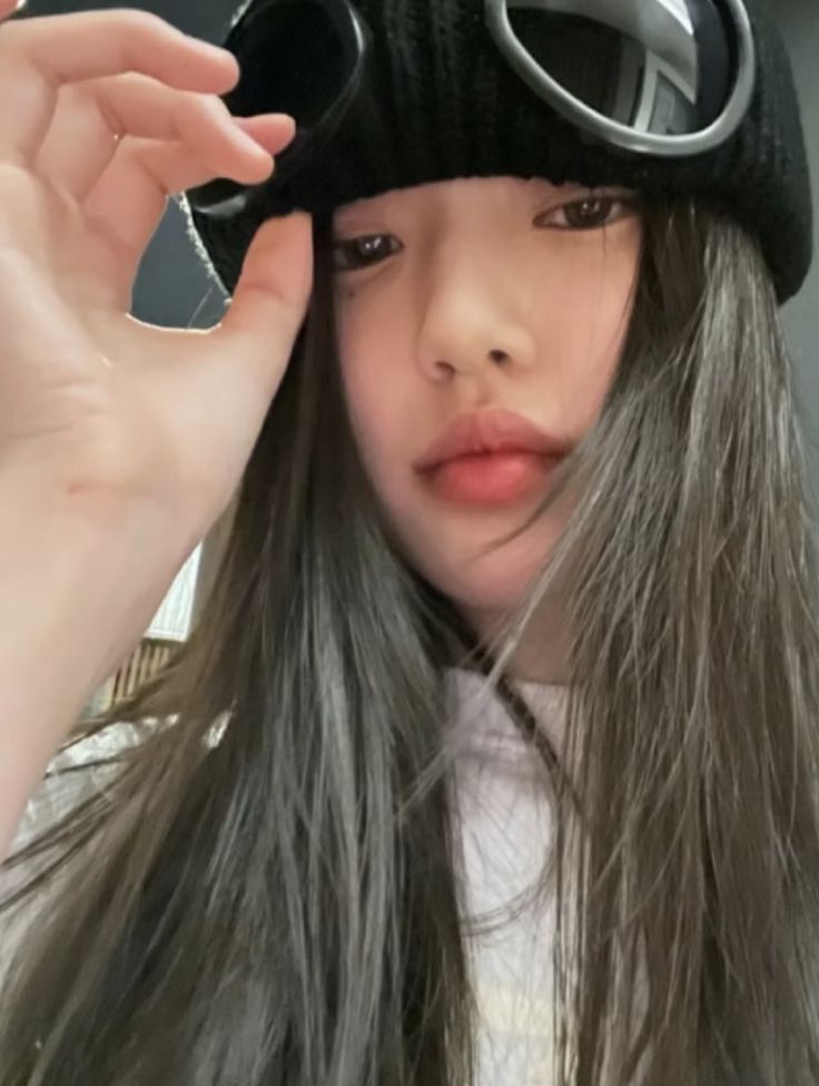 a girl with long gray hair wearing a black hat and goggles on her head