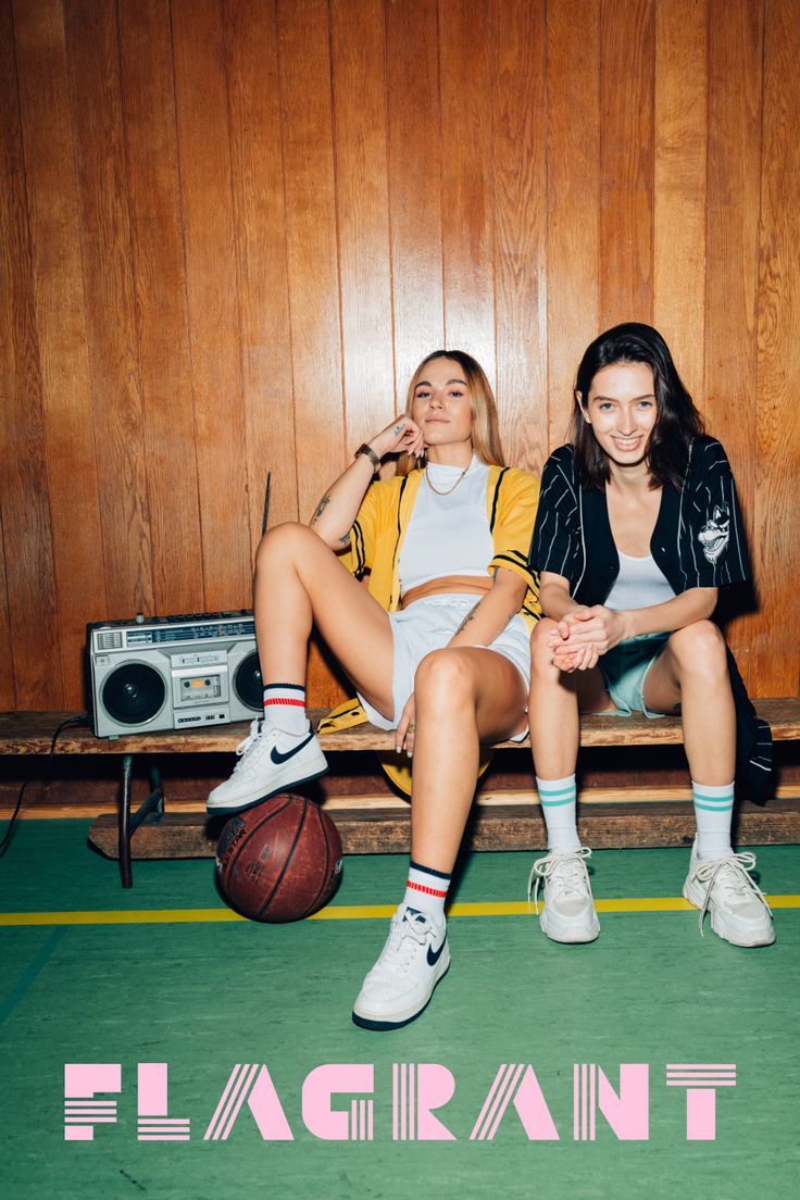 two young women sitting on a bench next to a basketball