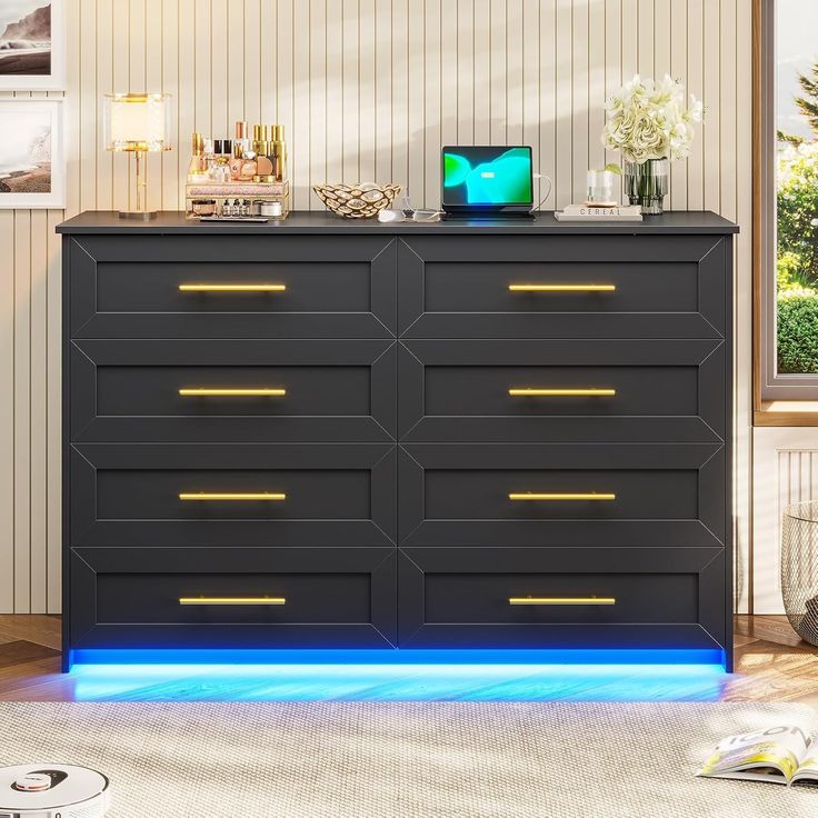 a black dresser with gold handles and blue light under the drawers is shown in front of a window